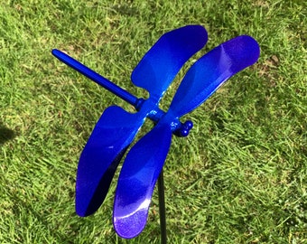 Pode incluir: Uma estaca de jardim de metal azul em forma de libélula com um degradê de cor que vai do azul escuro ao azul claro. A libélula está pousada com as asas abertas.