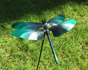 Pode incluir: Uma estaca de jardim de metal preto em forma de libélula com asas de glitter verde. As asas têm um degradé de verde para preto.