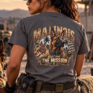May include: A charcoal gray t-shirt featuring a graphic of two Belgian Malinois dogs, palm trees, and the text "MALINOIS" and "BUILT FOR THE MISSION" with "TRAIN WORK DRIVE REPEAT" printed on the back, worn with olive green tactical pants.
