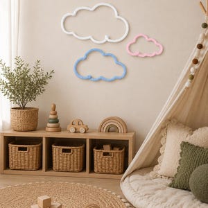 May include: A child's room scene featuring three cloud-shaped wall decorations in white, blue, and pink. A wooden shelf displays woven baskets, wooden toys, and a potted plant. A round jute rug and a play tent create a cosy atmosphere.
