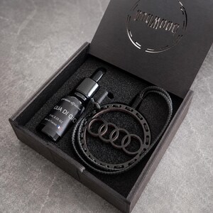 Peut inclure: Un coffret cadeau en bois noir contenant un flacon de parfum Aqua Di Gio de 10 ml et un pendentif circulaire noir arborant le logo Audi à quatre anneaux. Le couvercle de la boîte présente une découpe circulaire et l'intérieur est en mousse.