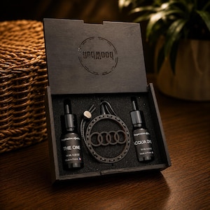 Peut inclure: Un coffret cadeau en bois noir contenant deux flacons compte-gouttes en verre de 10 ml étiquetés THE ONE et ACQUA DI G, ainsi qu'un désodorisant de voiture circulaire en bois avec le logo Audi. Le couvercle porte le texte unqmooq.