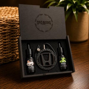 Peut inclure: Un coffret cadeau en bois noir contenant deux flacons compte-gouttes en verre de 10 ml et un pendentif circulaire noir avec le logo Honda sur un cordon. La bouteille de gauche est étiquetée Coffee et celle de droite Mojito.
