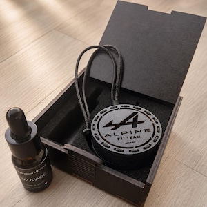 Peut inclure: Une boîte en bois noir contenant un désodorisant suspendu circulaire noir avec le logo et le texte Alpine F1 Team. À côté de la boîte se trouve un petit flacon compte-gouttes en verre ambré étiqueté Sauvage avec un bouchon noir, contenant 10 ml.