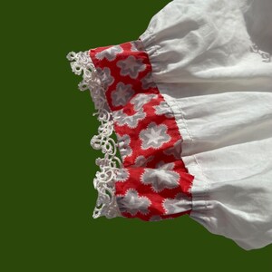 Peut inclure: Tissu de coton blanc avec une bordure florale rouge et blanche. La bordure est orn&eacute;e d'une dentelle blanche.