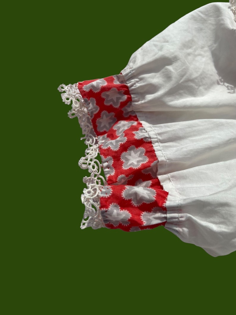 Peut inclure: Tissu de coton blanc avec une bordure florale rouge et blanche. La bordure est orn&eacute;e d'une dentelle blanche.