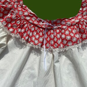 Peut inclure: Chemise blanche avec un col &agrave; volants imprim&eacute; floral rouge et blanc et une bordure en dentelle blanche. Le col est dot&eacute; d'un ruban blanc.