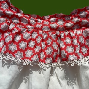 Peut inclure: Une robe en coton blanc avec un volant &agrave; l'encolure imprim&eacute; de fleurs rouges et blanches. Le volant est bord&eacute; de dentelle blanche.