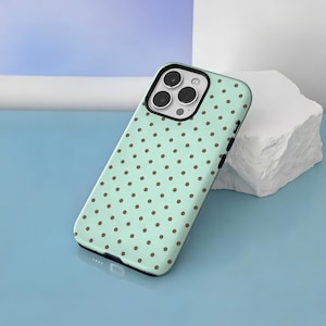 May include: A mint green smartphone case featuring a repeating pattern of small brown polka dots. The case has a black camera cutout frame with three circular lens openings and a small flash aperture, designed to fit a modern smartphone model.