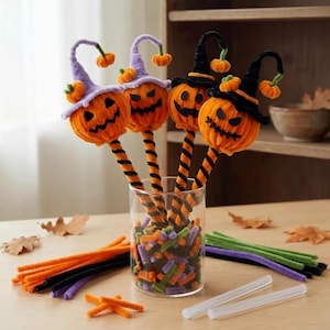 May include: Four orange chenille pumpkin toppers with black felt faces, two wearing lavender witch hats and two wearing black witch hats, attached to orange and black striped stems, displayed in a clear glass jar filled with colorful craft pieces.