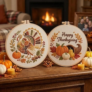 Puede incluir: Dos bastidores de bordado circulares con paneles de tela y motivos otoñales. Un bastidor muestra un pavo rodeado de hojas y calabazas, mientras que el otro presenta el texto Happy Thanksgiving con calabazas y un cuerno de la abundancia.
