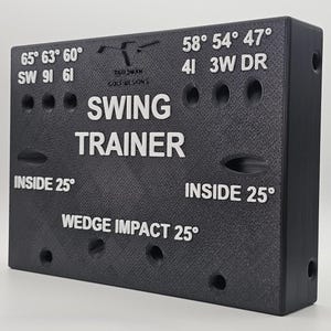 May include: A black rectangular golf swing trainer with white text and markings. The device features labels including SW, 6I, 4I, 3W, DR, and various degree angles. The center displays the words SWING TRAINER and WEDGE IMPACT 25 degrees.