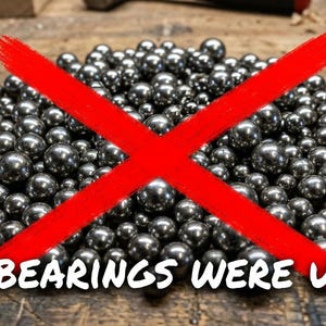 May include: A large pile of small, polished, spherical silver-colored metal ball bearings arranged in a mound. A bold, bright red X is superimposed over the center of the pile, and the text NO BEARINGS WERE USED! is printed in white at the bottom.