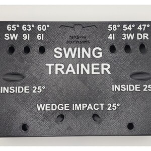 May include: A black rectangular golf swing trainer board with a textured surface. It features white printed text including SWING TRAINER, WEDGE IMPACT 25&deg;, INSIDE 25&deg;, and various degree markings like 65&deg;, 63&deg;, 60&deg;, 58&deg;, 54&deg;, 47&deg; with corresponding club labels.