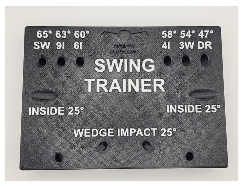 May include: A black rectangular golf swing trainer board with a textured surface. It features white printed text including SWING TRAINER, WEDGE IMPACT 25&deg;, INSIDE 25&deg;, and various degree markings like 65&deg;, 63&deg;, 60&deg;, 58&deg;, 54&deg;, 47&deg; with corresponding club labels.