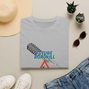 May include: A heather gray t-shirt featuring a black tire track graphic running diagonally across the chest. The text FUTURE ROADKILL is printed in blue with a yellow outline, positioned above a red triangular warning sign with a deer silhouette.