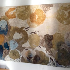 May include: Large abstract wall art featuring a textured design with circular shapes in shades of blue, brown, and gold. The artwork is mounted on a white wall, adding a touch of modern decor to the space. The piece is a unique, eye-catching addition to any room.