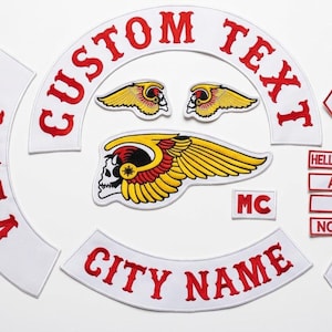 May include: A set of embroidered patches featuring white fabric with red lettering. Includes curved rockers with CUSTOM TEXT and CITY NAME, a central winged skull emblem, two small wing patches, an MC patch, and rectangular bars reading HELLS ANGELS, AFFA, 666, NOMADS, plus two diamond-shaped 1% patches.