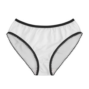 Op de afbeelding: Witte onderbroek met zwarte kanten rand. De slip heeft een klassieke snit en is gemaakt van een gladde, ondoorzichtige stof. De tailleband en beenopeningen zijn afgewerkt met delicate zwarte kant.