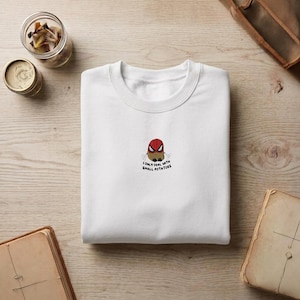 May include: A white crewneck sweatshirt featuring a small embroidered graphic in the center. The design depicts a brown potato wearing a red superhero mask with black eye details. Below the potato, the text reads, I ONLY DEAL WITH SMALL POTATOES.