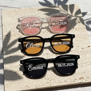 May include: Three pairs of sunglasses with clear, black, and black frames. The lenses feature white printed text: the top pair says Sophia 06.15.2026, the middle pair says Olivia 06.15.2026, and the bottom pair says Emma 06.15.2026.
