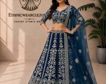 Peut inclure: Un ensemble lehenga choli bleu profond orné de broderies argentées complexes sur la jupe et le chemisier court. La tenue comprend un dupatta bleu transparent assorti avec des motifs floraux argentés et une bordure décorative travaillée.