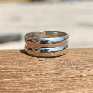 Peut inclure: Une bague de couleur argentée polie avec un anneau lisse et arrondi. La surface métallique est hautement réfléchissante, présentant des reflets lumineux et un profil incurvé. La bague présente un design circulaire simple et continu.