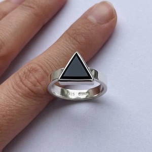 May include: A sterling silver ring featuring a prominent triangular black stone set in the center. The inner band of the ring is clearly stamped with the hallmark 925, indicating the silver content of this polished metal jewelry piece.