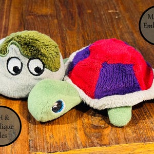 May include: A plush turtle toy with a light green head and a multi-coloured shell featuring red and purple segments. The turtle has large embroidered eyes. Text on the image reads Machine Embroidery Files and ITH & Applique Files.