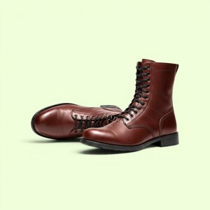 Puede incluir: Un par de botas con cordones hasta la media pantorrilla en cuero liso de color marrón oscuro. Estas botas cuentan con una punta redondeada, cordones negros a través de ojales metálicos, una caña estructurada y un tacón plano negro con suela de goma.