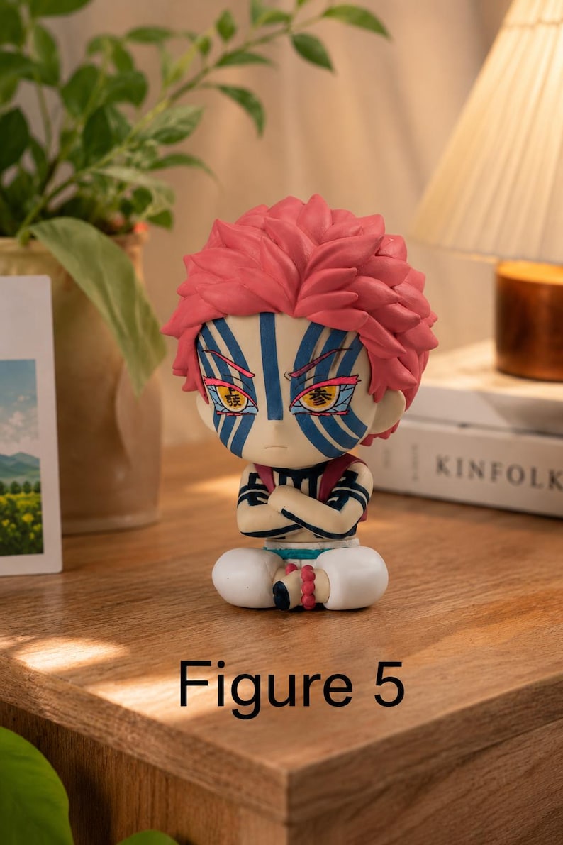 Puede incluir: Figura detallada de un personaje con pelo rosa puntiagudo, marcas faciales azules y blancas y brazos cruzados. La figura est&aacute; sentada con pantalones blancos y una pulsera de cuentas rojas. El texto "Figure 5" est&aacute; en la base.