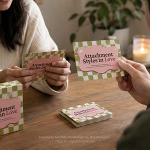 May include: A deck of cards titled "Attachment Styles in Love" with a pink and green checkered design. The cards are being held by people. The text "Attachment Styles in Love" is visible on the cards and the box.