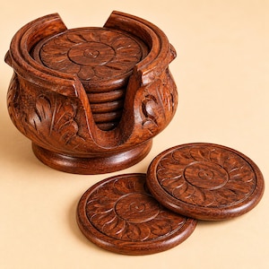 May include: A set of circular dark brown wooden coasters featuring a carved floral petal pattern. The coasters are stored in a matching carved wooden holder with a wide opening, and two additional coasters are placed in front of the holder.