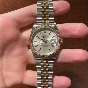 May include: A silver and gold Rolex Oyster Perpetual Datejust watch. The watch has a silver dial with a date window at 3 o'clock. It features a fluted bezel and a two-tone Jubilee bracelet.