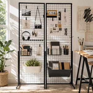May include: Two tall black metal grid panels standing side-by-side, featuring various hanging accessories including wire baskets, a white planter with a green plant, a black storage bin, clips holding photos, a camera, headphones, and a calendar.
