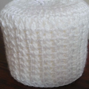 May include: White crocheted toilet paper roll cover. The cover is made with a simple stitch pattern.