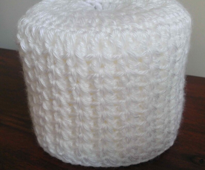 May include: White crocheted toilet paper roll cover. The cover is made with a simple stitch pattern.