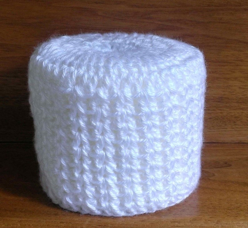 May include: White crocheted toilet paper roll cover. The cover is made with a simple stitch pattern and has a smooth, soft texture.