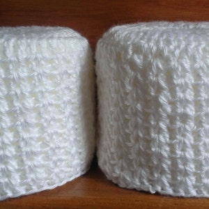 May include: Two white crocheted toilet paper roll covers. The covers are made with a simple stitch pattern and have a slightly textured look.