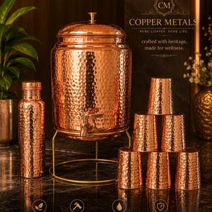 May include: A copper water dispenser with a hammered texture, a matching bottle, and six copper cups. The dispenser has a spigot and sits on a gold-colored stand. The image also includes text that reads "COPPER METALS" and "100% PURE COPPER."