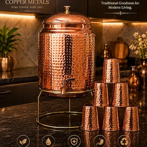 May include: A copper water dispenser with a hammered texture, a spigot, and a lid, displayed with matching copper cups. The dispenser sits on a gold-colored stand. The image includes text that reads "Pure Copper. Pure Wellness."