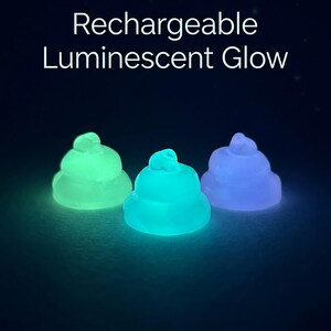 May include: Three small, rounded, pile-shaped objects that emit light in green, cyan, and purple. The text "Rechargeable Luminescent Glow" is displayed in white above the objects against a dark background. Each object has a smooth, translucent texture.