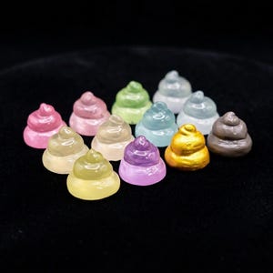 May include: A collection of twelve small, swirl-shaped figurines in various colors including pink, green, blue, yellow, purple, gold, and brown. Each figurine features a smooth, glossy finish and a rounded, stacked design with a pointed top.