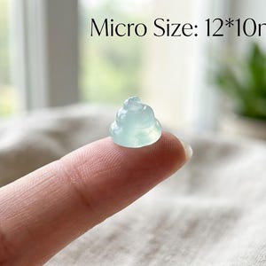 May include: A small, translucent, pale green carved figurine shaped like a coiled pile, measuring 12 by 10 millimeters. The object has a smooth, polished surface and a rounded, tiered form, displayed clearly against a neutral, soft-textured background.