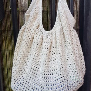 May include: A large, off-white crocheted tote bag with a wide, open top and two long straps. The bag is made with a simple, open stitch pattern and has a slightly rounded bottom.
