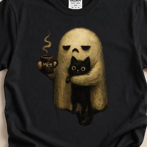 Op de afbeelding: Een zwart T-shirt met korte mouwen en een afbeelding van een beige geest die een zwarte kat en een bruine mok met de tekst "MEH" vasthoudt. De geest heeft een norse uitdrukking en er stijgt stoom op uit de mok. Het shirt heeft een Gildan label.