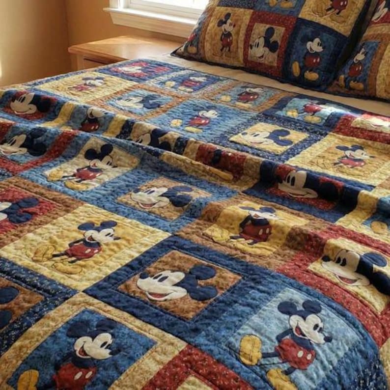 May include: A quilted bedspread and matching pillow sham featuring a patchwork grid pattern. Each square displays a printed illustration of Mickey Mouse in various poses against backgrounds of blue, yellow, and red with subtle textured patterns.