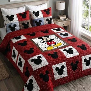 May include: Red and white Mickey Mouse themed quilt set with matching pillow shams. The quilt features a large Mickey Mouse character in the center, surrounded by black Mickey Mouse head silhouettes and white squares. The set is designed for a bed.