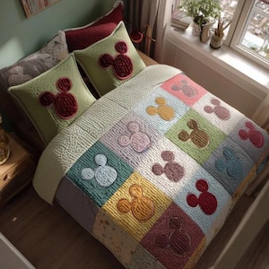 Op de afbeelding: Een bed met een patchwork quilt en twee bijpassende kussens. De quilt heeft een herhalend patroon van Mickey Mouse-hoofden in verschillende kleuren. De kussens zijn lichtgroen met een rode Mickey Mouse-kop.