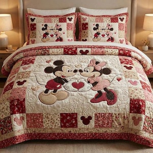 May include: A quilted bedspread and two pillow shams featuring Mickey and Minnie Mouse. The bedding has a patchwork design with red, pink, and cream squares. Mickey and Minnie are embroidered on the quilt, holding a heart. The pillow shams have the same design.